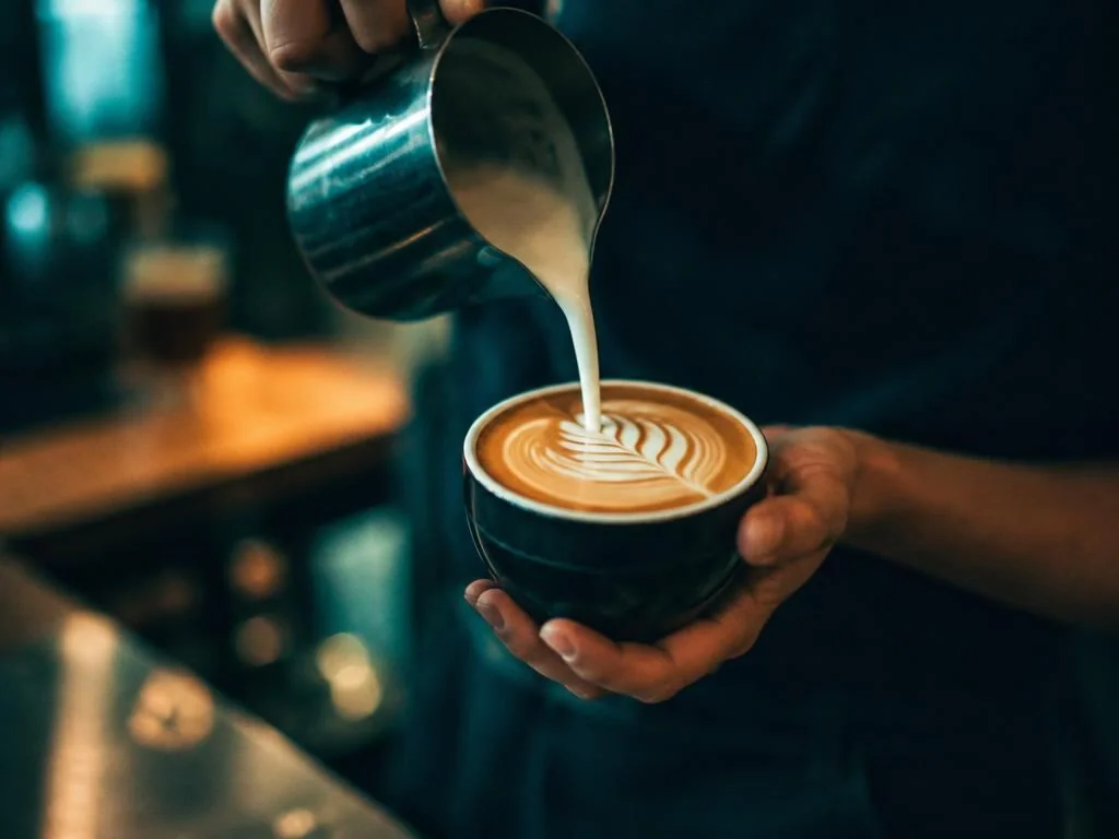 Barista's hands pouring latte art in a coffee shop