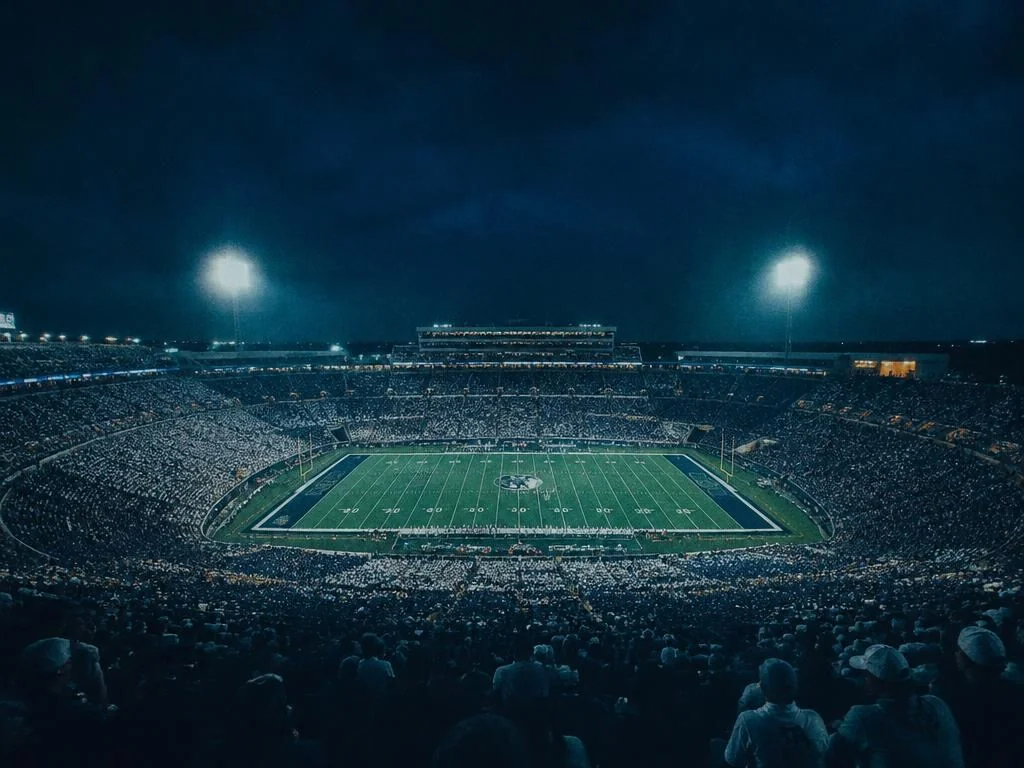 Wide view of a packed college football stadium at kickoff